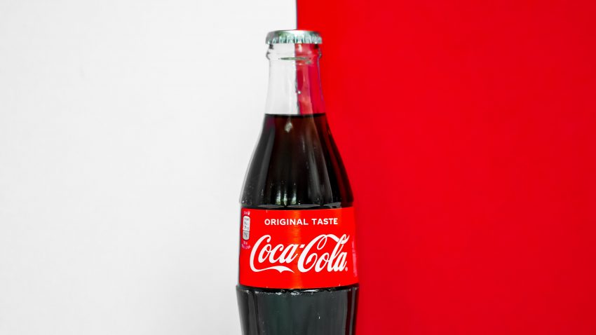 A Coca-Cola bottle over separated red and white backgrounds, a visual manifestation of their hybrid brand architecture.